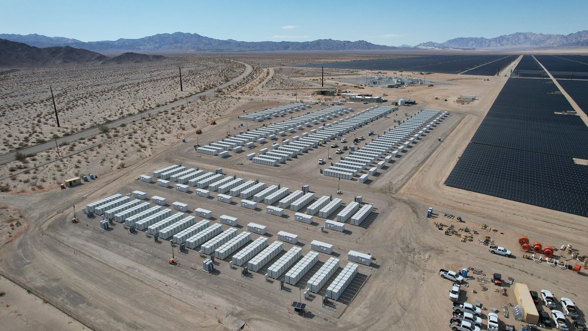 Containerised battery storage beside a solar plant, holding daytime power for the evening peak.